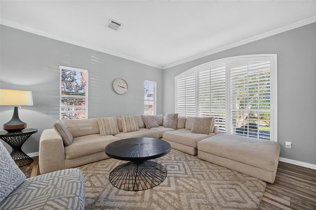 Neutral-toned living space featuring wood-finish flooring, crown molding, and an expansive arched window assembly equipped with integrated plantation shutters