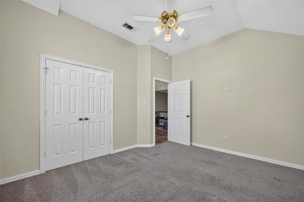 Vaulted ceilings, neutral wall palette, wall-to-wall carpeting, four-blade ceiling fan with integrated lighting, and dual-panel closet doors