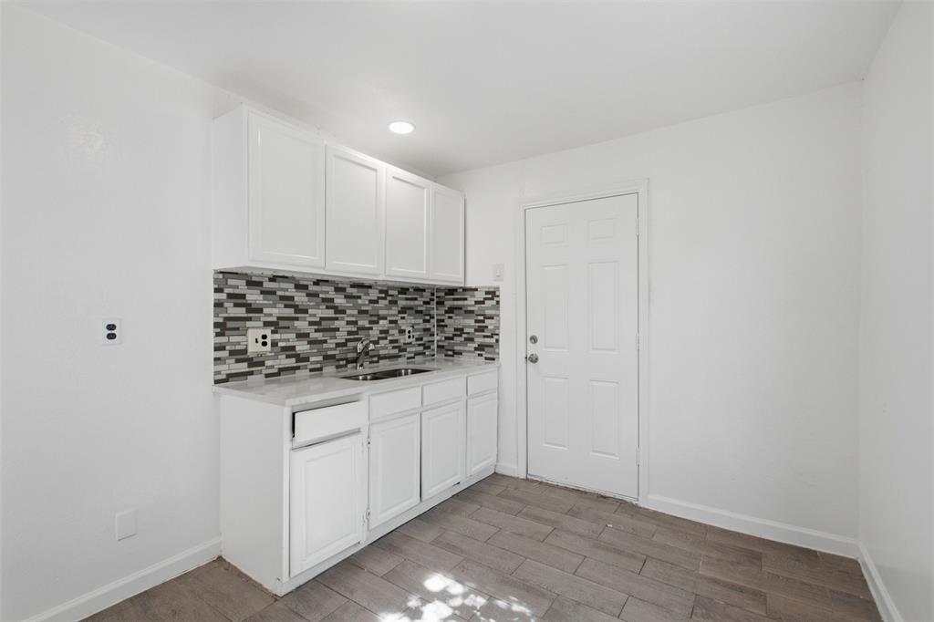 White cabinetry with stone-finish countertops, multi-tonal linear tile backsplash, stainless steel sink, and wood-finish flooring