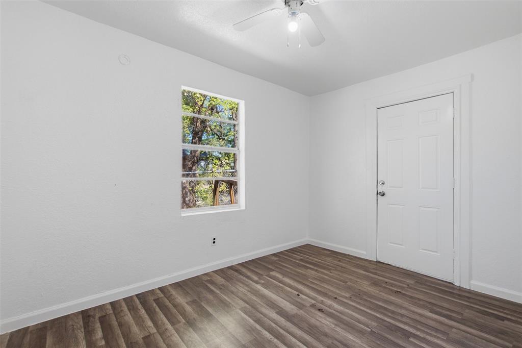 Neutral-toned room featuring wood-finish flooring, a six-panel door, and a ceiling-mounted light fixture with an integrated fan
