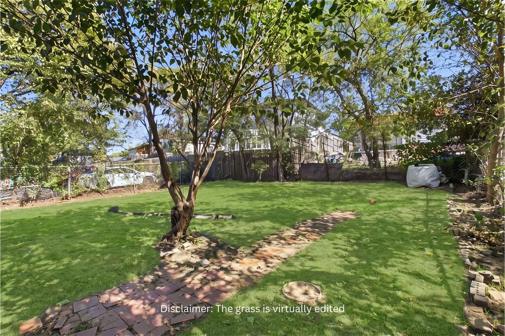 Expansive backyard featuring a lush lawn, mature trees, and a brick-paver pathway