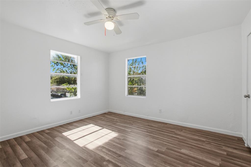 Room featuring wood-finish flooring, crisp white walls, dual windows, and a ceiling-mounted light fixture with a fan