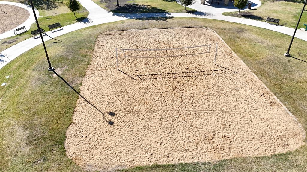 Sand volleyball court featuring a tensioned net, perimeter lighting poles, and concrete paved walkways