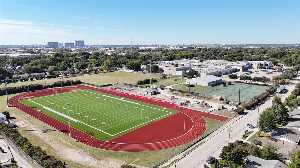 Aerial perspective featuring an artificial turf football field, multi-lane track, and paved tennis courts