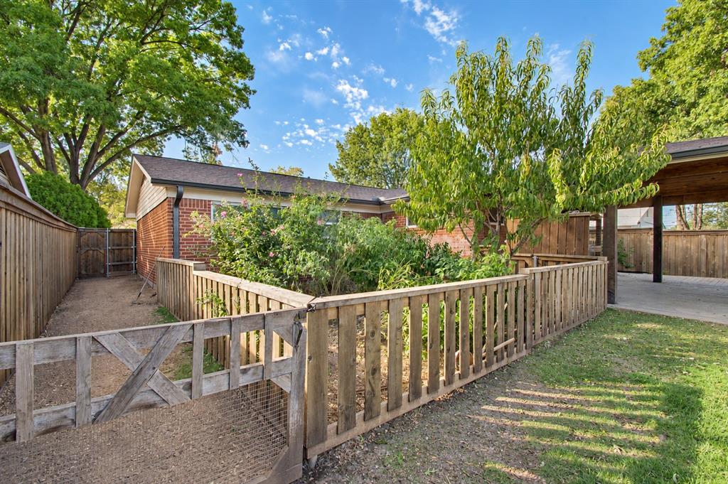 Backyard area featuring a wooden picket fence enclosure, brick exterior wall, covered patio space, and perimeter wooden privacy fencing