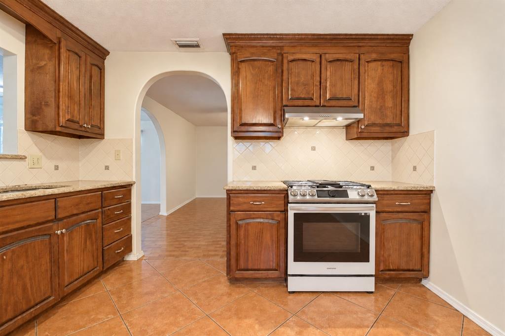 Kitchen featuring raised-panel wood cabinetry, stone countertops, diamond-pattern tile backsplash, stainless steel gas range, and diagonal tile flooring