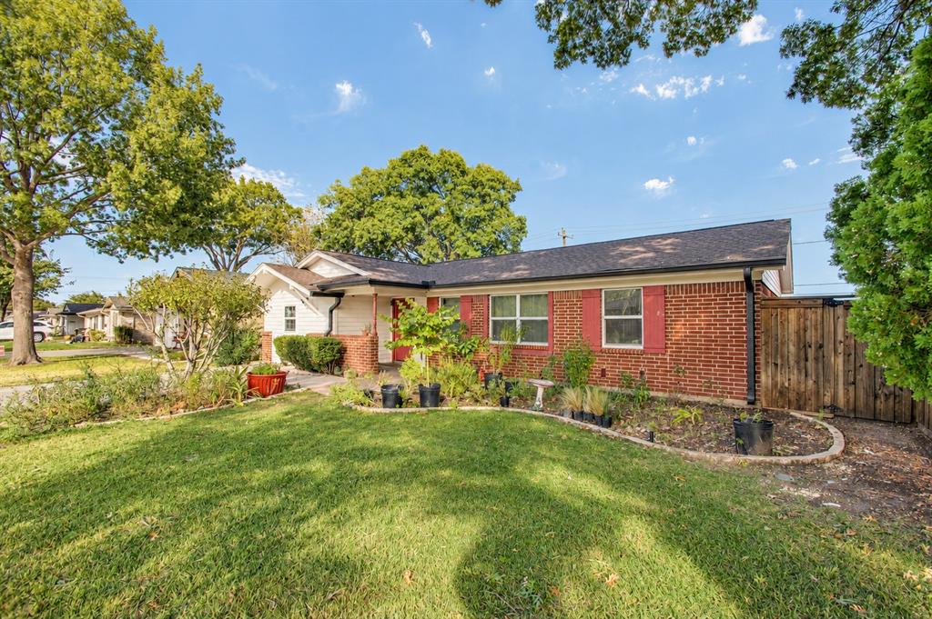 Single-story brick exterior featuring a shingled gable roof, red shutters, and an expansive lawn with manicured landscaping and wood fencing