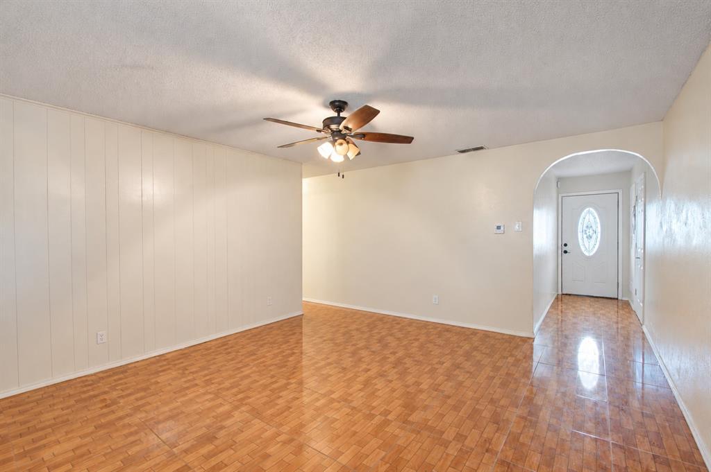Interior space featuring wood-finish flooring, a ceiling fan with multi-light fixture, vertical paneling, and an arched entryway with an exterior door containing an oval glass insert