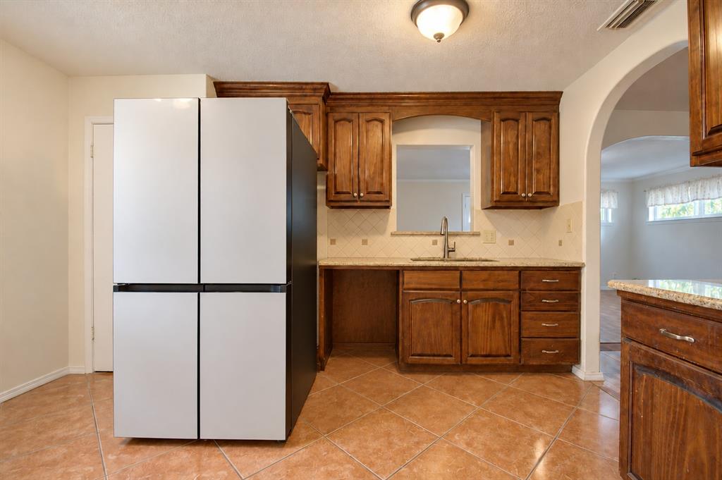 Kitchen featuring stained wood cabinetry, stone-finish countertops, ceramic tile flooring, a pass-through window, and an arched entry