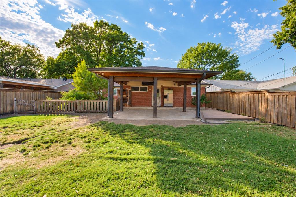 Rear exterior featuring a covered patio, brick siding, concrete hardscaping, and wood fencing