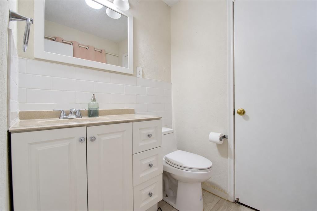 White vanity cabinet featuring decorative hardware, rectangular countertop with integrated sink, white subway tile backsplash, wall-mounted mirror, and polished chrome fixtures