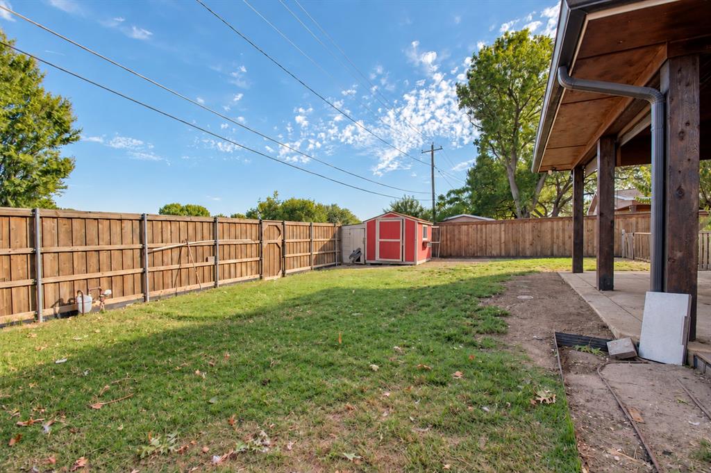 Fenced backyard featuring a covered patio, grass lawn, and a detached storage structure