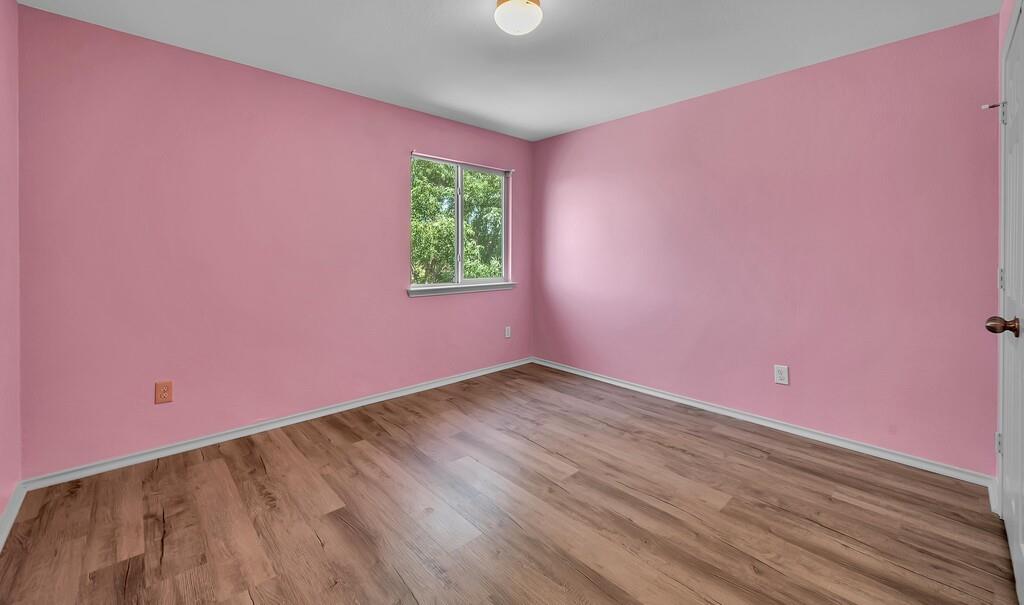 Wood-finish flooring, single window with exterior scenery, flush-mount ceiling lighting, and multi-panel interior door