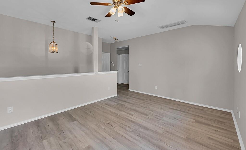 Vaulted ceilings, wood-finish flooring, half-wall partition, integrated ceiling fan with light fixture, and pendant lighting