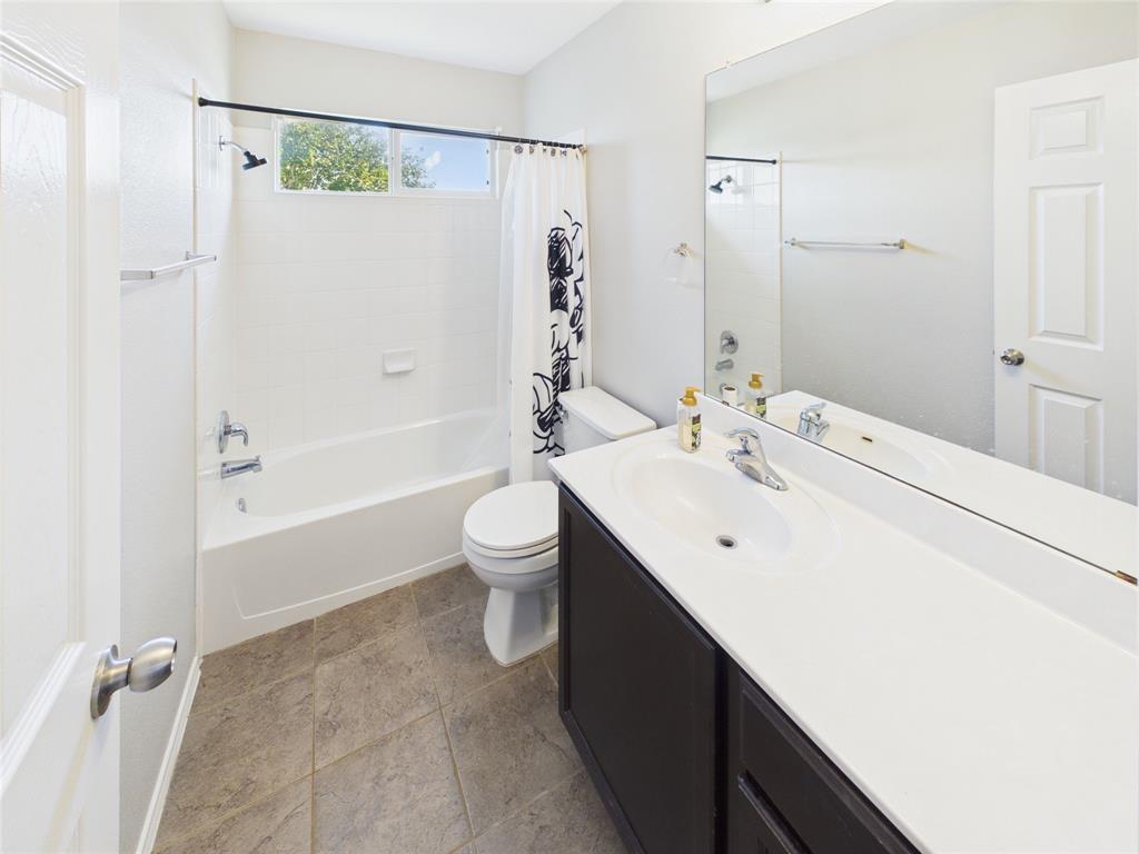 Upstairs Full bathroom featuring a dark-finish vanity with an integrated white countertop, a large wall-mounted mirror, a porcelain tub-and-shower combination, and tiled flooring