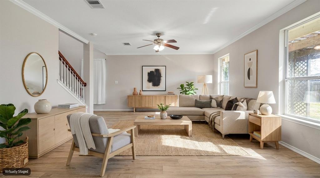 Living area featuring wood-finish flooring, crown molding, a central ceiling fan with integrated lighting, and multiple windows Living area featuring wood-finish flooring, crown molding, a central ceiling fan with integrated lighting, and multiple windows