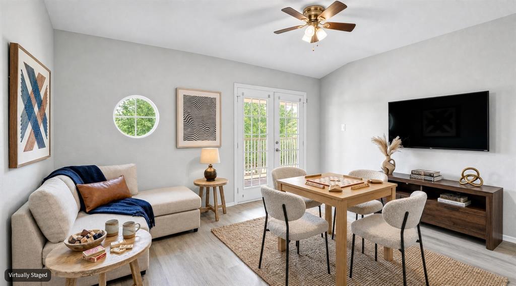 VIRTUALLY STAGED Light-filled interior featuring wood-finish flooring, a unique circular accent window, and double French doors leading to an exterior deck, finished with a central ceiling fan light fixture