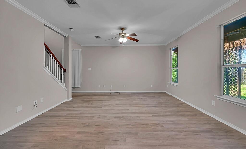 Neutral-toned interior featuring wood-finish flooring, crown molding, a ceiling fan with integrated lighting, and a staircase with a wooden handrail and white balusters Neutral-toned interior featuring wood-finish flooring, crown molding, a ceiling fan with integrated lighting, and a staircase with a wooden handrail and white balusters