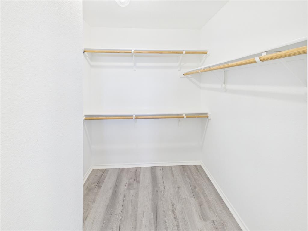 Walk-in closet featuring wood-finish flooring, white walls, and tiered metal shelving with natural wood-tone rods