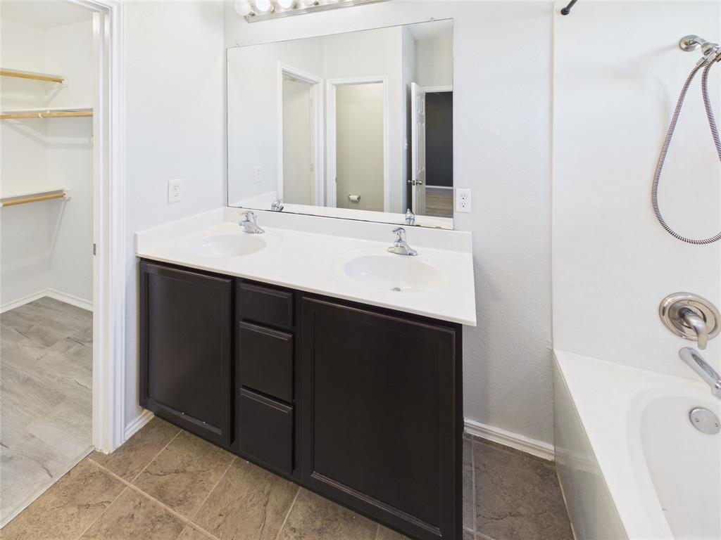 Dual-sink vanity with dark cabinetry, white solid-surface countertop, full-width vanity mirror, and attached walk-in closet with integrated shelving
