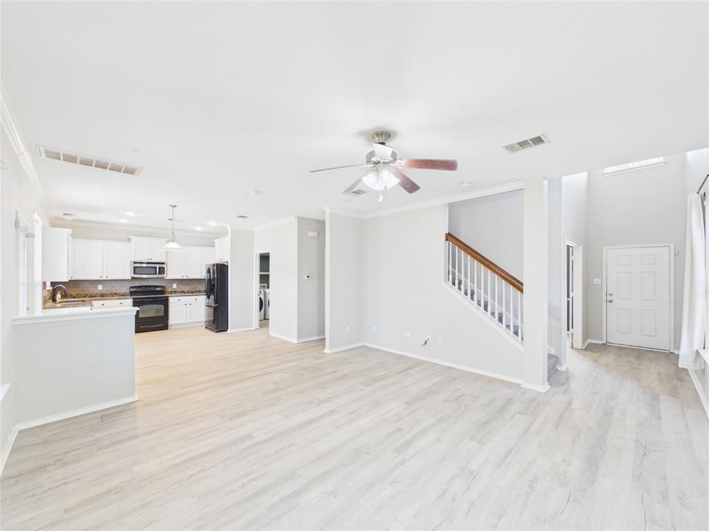 Open floor plan featuring wood-finish flooring, kitchen cabinetry with neutral-tone countertops, a ceiling fan, and a staircase with a wooden handrail Open floor plan featuring wood-finish flooring, kitchen cabinetry with neutral-tone countertops, a ceiling fan, and a staircase with a wooden handrail
