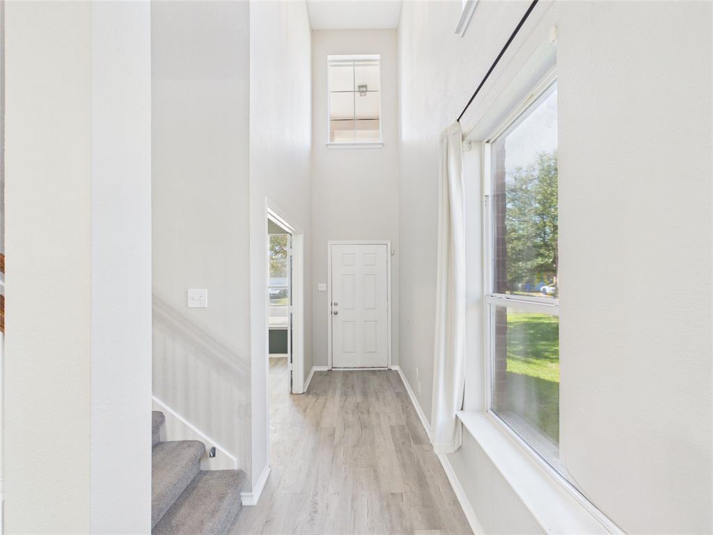 Entryway featuring high ceilings, wood-finish flooring, a tall transom window, and a staircase with carpeted treads Entryway featuring high ceilings, wood-finish flooring, a tall transom window, and a staircase with carpeted treads