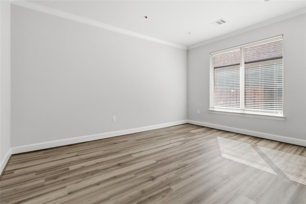 Neutral interior featuring wood-finish flooring, crisp crown molding, and large window with horizontal blinds