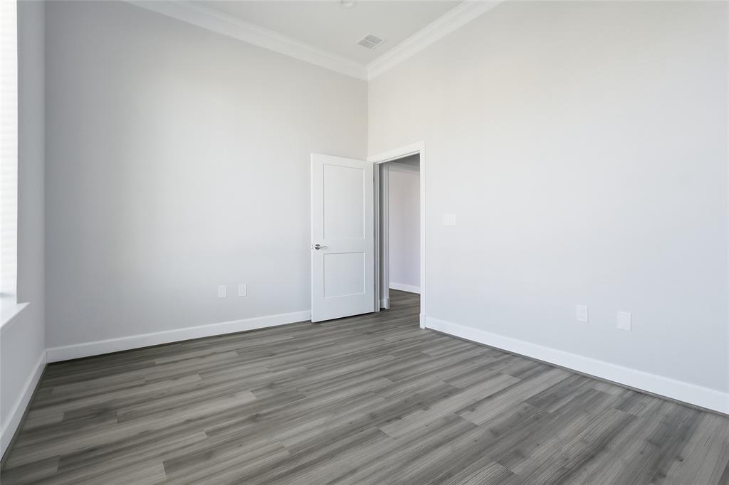 High-ceiling room featuring wood-finish flooring, crown molding, and a paneled interior door High-ceiling room featuring wood-finish flooring, crown molding, and a paneled interior door