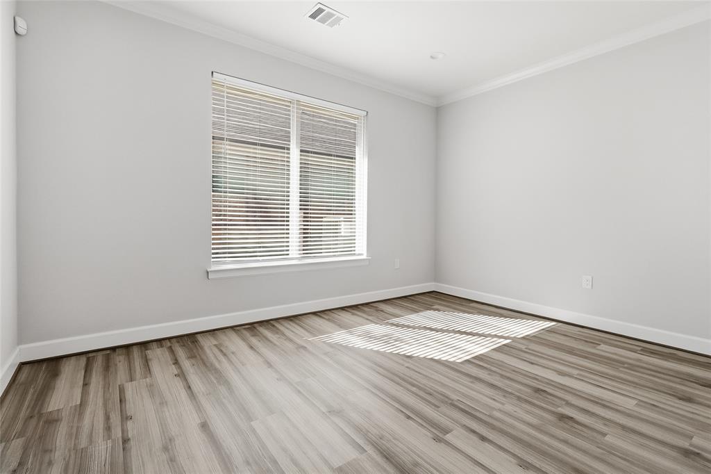 Neutral-toned interior featuring wood-finish flooring, crown molding, and a large window with fitted blinds