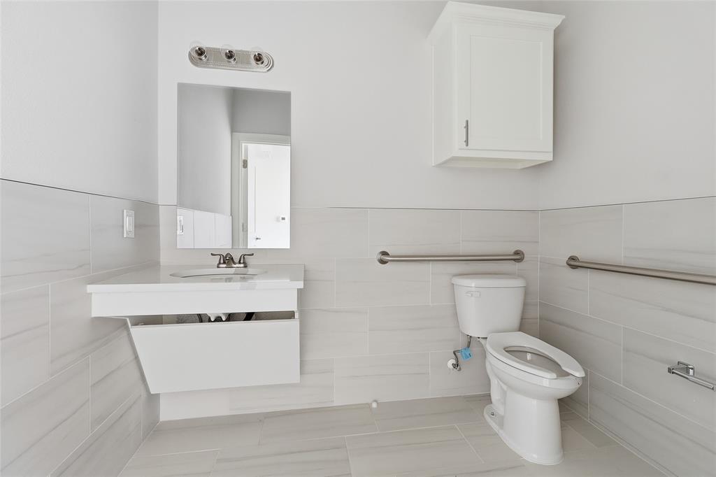 Wall-mounted vanity with rectangular sink, white wall cabinet, horizontal tile wainscoting, and stainless steel grab bars