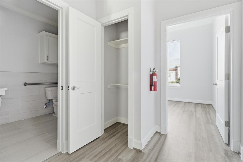 Interior hallway featuring wood-finish flooring, two-panel interior doors, recessed storage shelving, and light-toned tile flooring in the tiled room