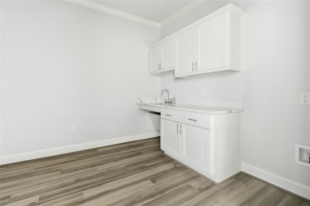 Built-in white cabinetry featuring shaker-style doors, stone-surface countertop, integrated sink with chrome faucet, and wood-finish flooring