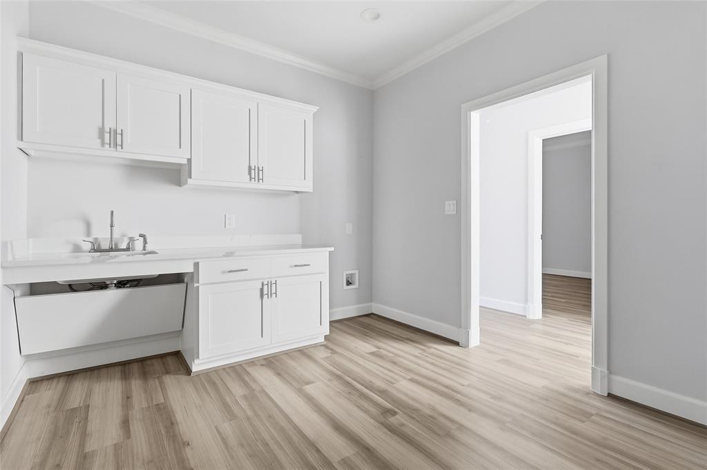 White cabinetry featuring brushed nickel hardware, stone-finish countertops, integrated sink, and wood-finish flooring