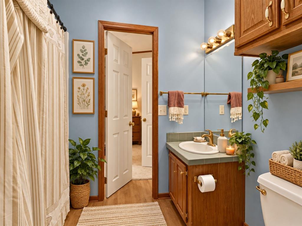 Bathroom featuring a wood-finish vanity with an integrated tile countertop, an oval undermount sink, brass-finish hardware, and built-in upper cabinetry