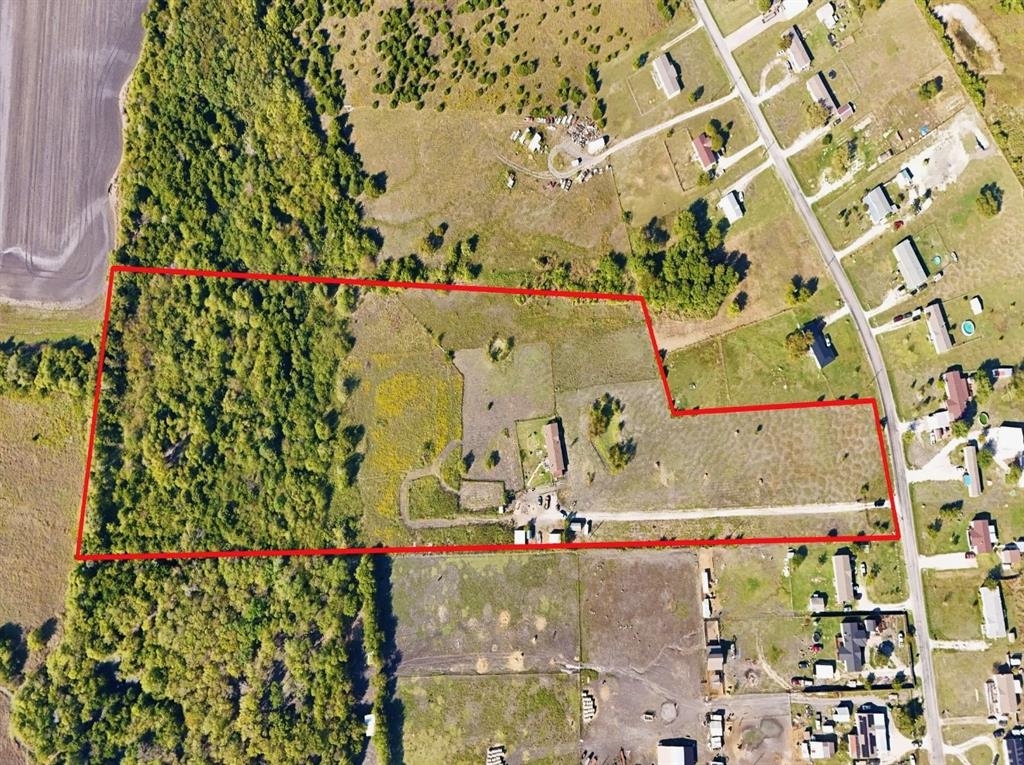 Aerial perspective of expansive acreage featuring mature tree lines, open pasture, and a gravel driveway providing property access
