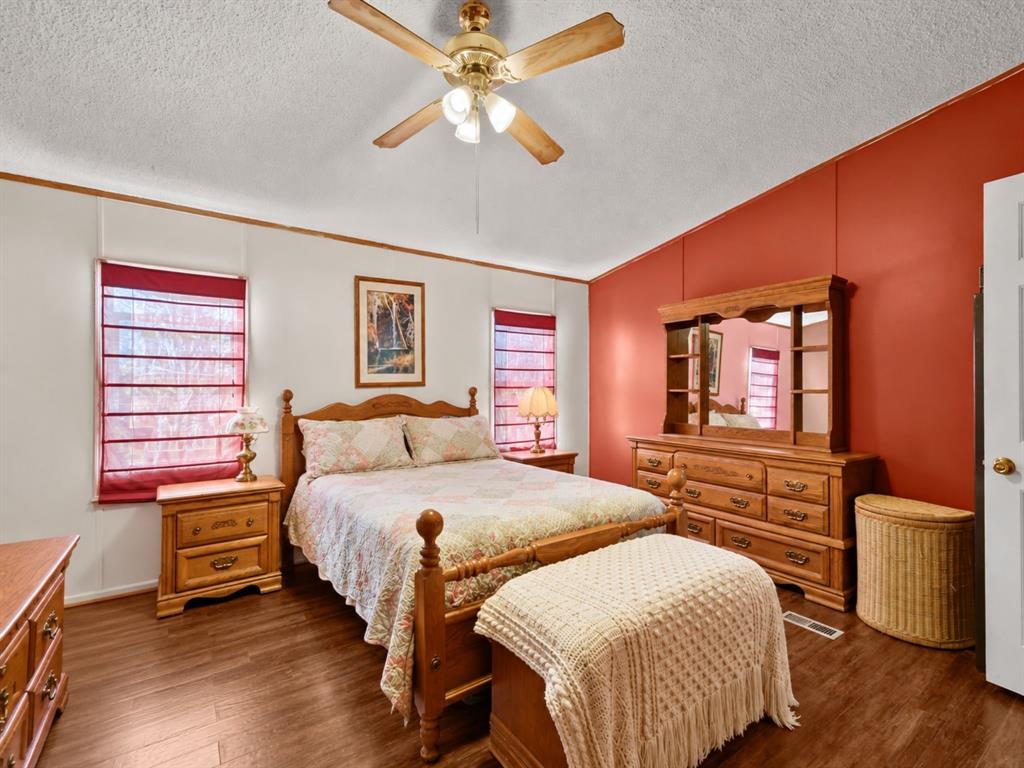 Vaulted ceiling with a centrally mounted wood-tone ceiling fan and light fixture, wood-finish flooring, and dual windows