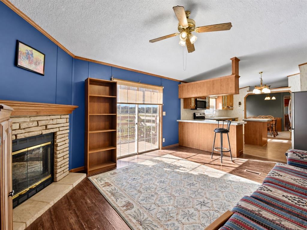 Stone fireplace with wood mantel, built-in shelving, sliding glass door, wood-finish flooring, and peninsula kitchen counter