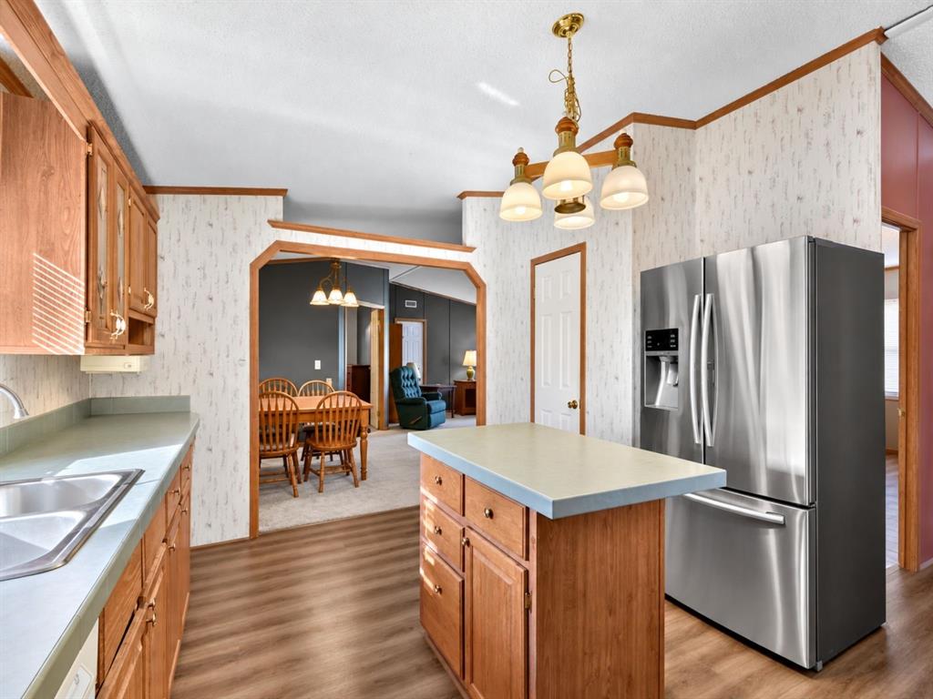 Kitchen featuring natural wood cabinetry, a center island with solid surface countertops, stainless steel French-door refrigerator, and wood-finish flooring