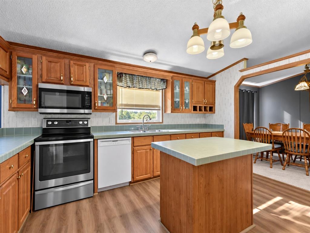 Kitchen featuring wood cabinetry, stainless steel appliances, tile countertops, a central island, and wood-finish flooring