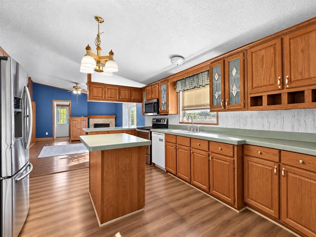 Kitchen featuring wood cabinetry, solid surface countertops, an integrated center island, stainless steel refrigerator, and wood-finish flooring