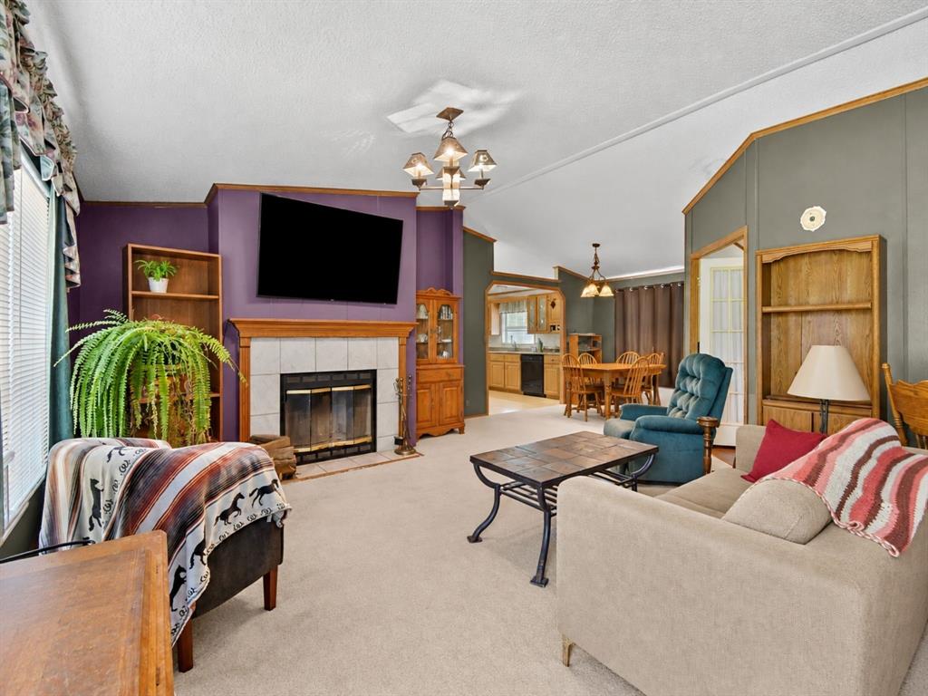 Living area featuring a tile-surround fireplace, built-in wooden shelving, vaulted ceilings, and multi-arm chandeliers