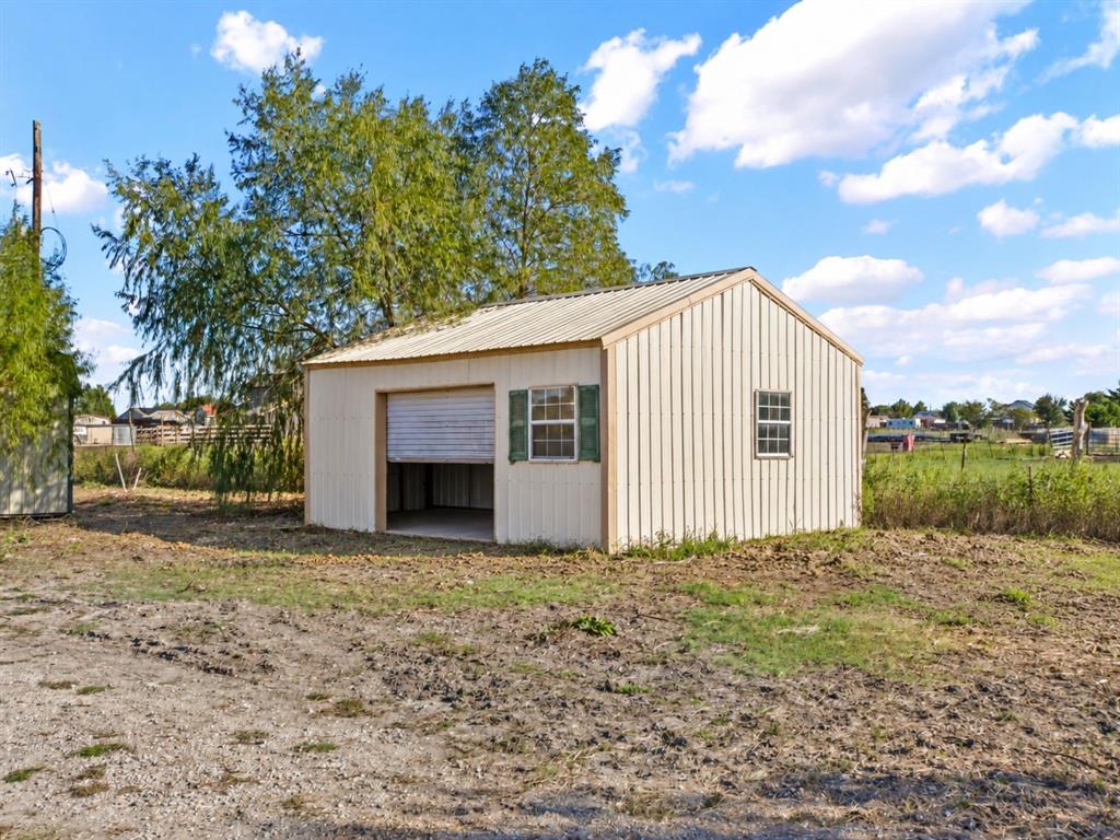 Detached metal-sided structure featuring a metal roof, roll-up garage door, and two shuttered windows