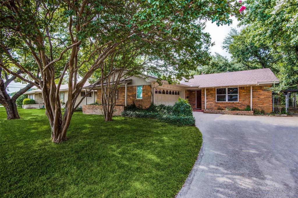 Brick exterior residence featuring an attached garage, paved driveway, mature trees, and landscaping Brick exterior residence featuring an attached garage, paved driveway, mature trees, and landscaping