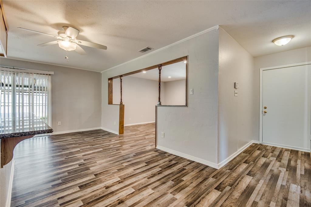 Interior space featuring wood-finish flooring, a ceiling fan with integrated lighting, recessed wall opening with decorative columns, and vertical blinds Interior space featuring wood-finish flooring, a ceiling fan with integrated lighting, recessed wall opening with decorative columns, and vertical blinds