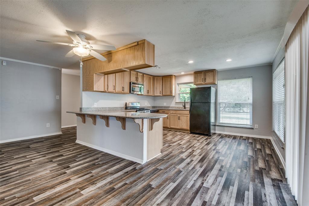 Kitchen featuring light wood-finish cabinetry, stone-composite countertops, wood-finish flooring, a breakfast bar, and a ceiling fan Kitchen featuring light wood-finish cabinetry, stone-composite countertops, wood-finish flooring, a breakfast bar, and a ceiling fan