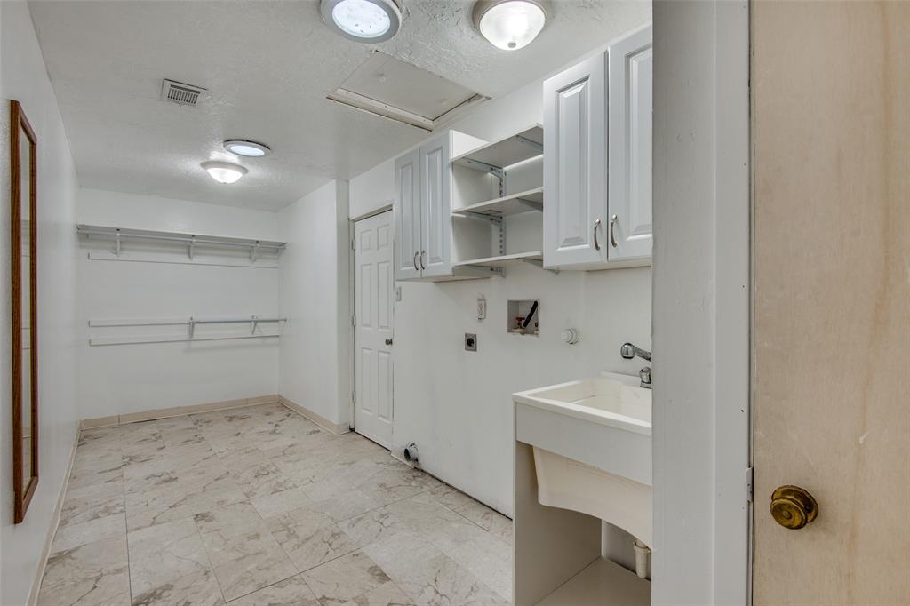Laundry room featuring stone-finish tile flooring, white cabinetry with open shelving, a utility sink, and wall-mounted storage racks