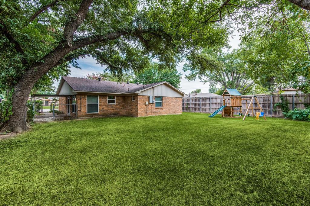 Expansive backyard featuring a manicured lawn, mature trees, wood privacy fencing, and a covered patio area