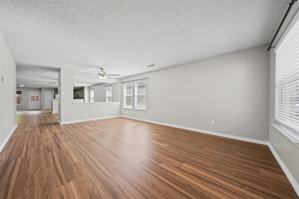 Open-concept interior featuring wood-finish flooring, neutral wall paint, multi-pane windows with horizontal blinds, and a ceiling-mounted light fixture Open-concept interior featuring wood-finish flooring, neutral wall paint, multi-pane windows with horizontal blinds, and a ceiling-mounted light fixture