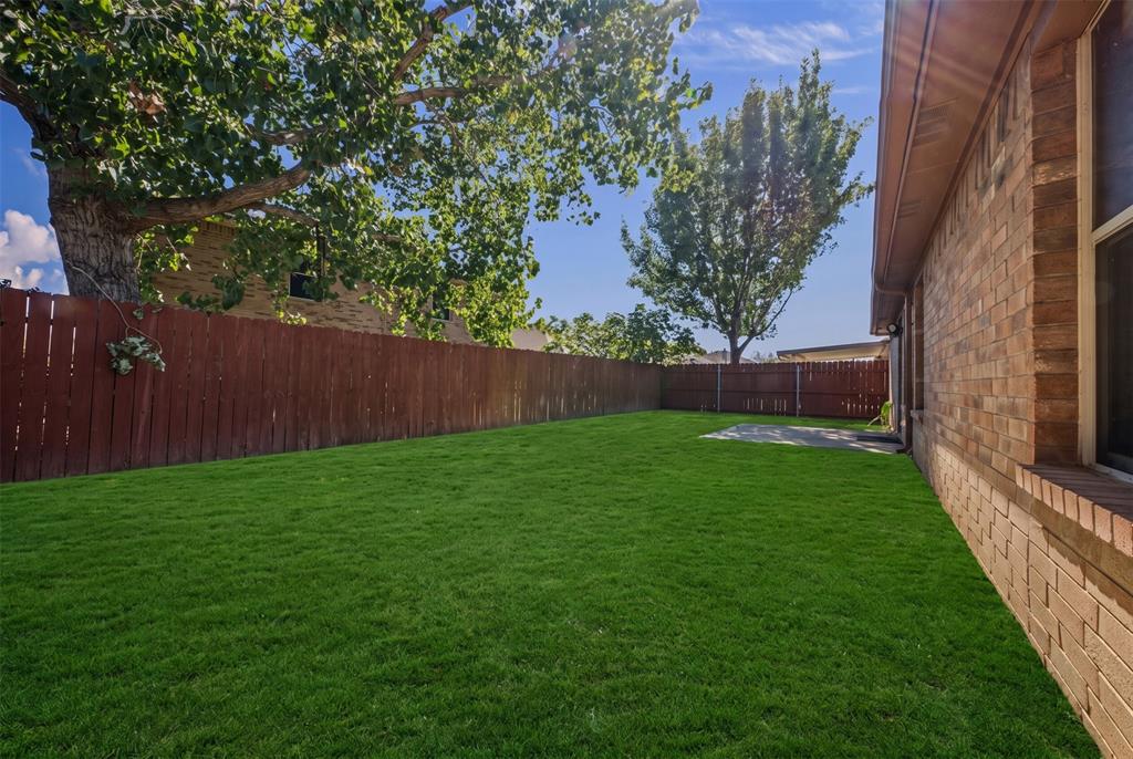 Private backyard featuring brick exterior siding, a level grass lawn, perimeter wood fencing, and mature trees