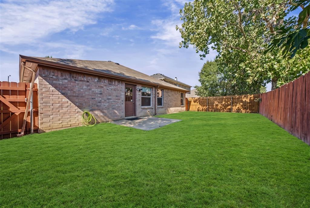 Rear exterior featuring brick siding, a concrete patio, and a fully enclosed wood fence surrounding a grass lawn